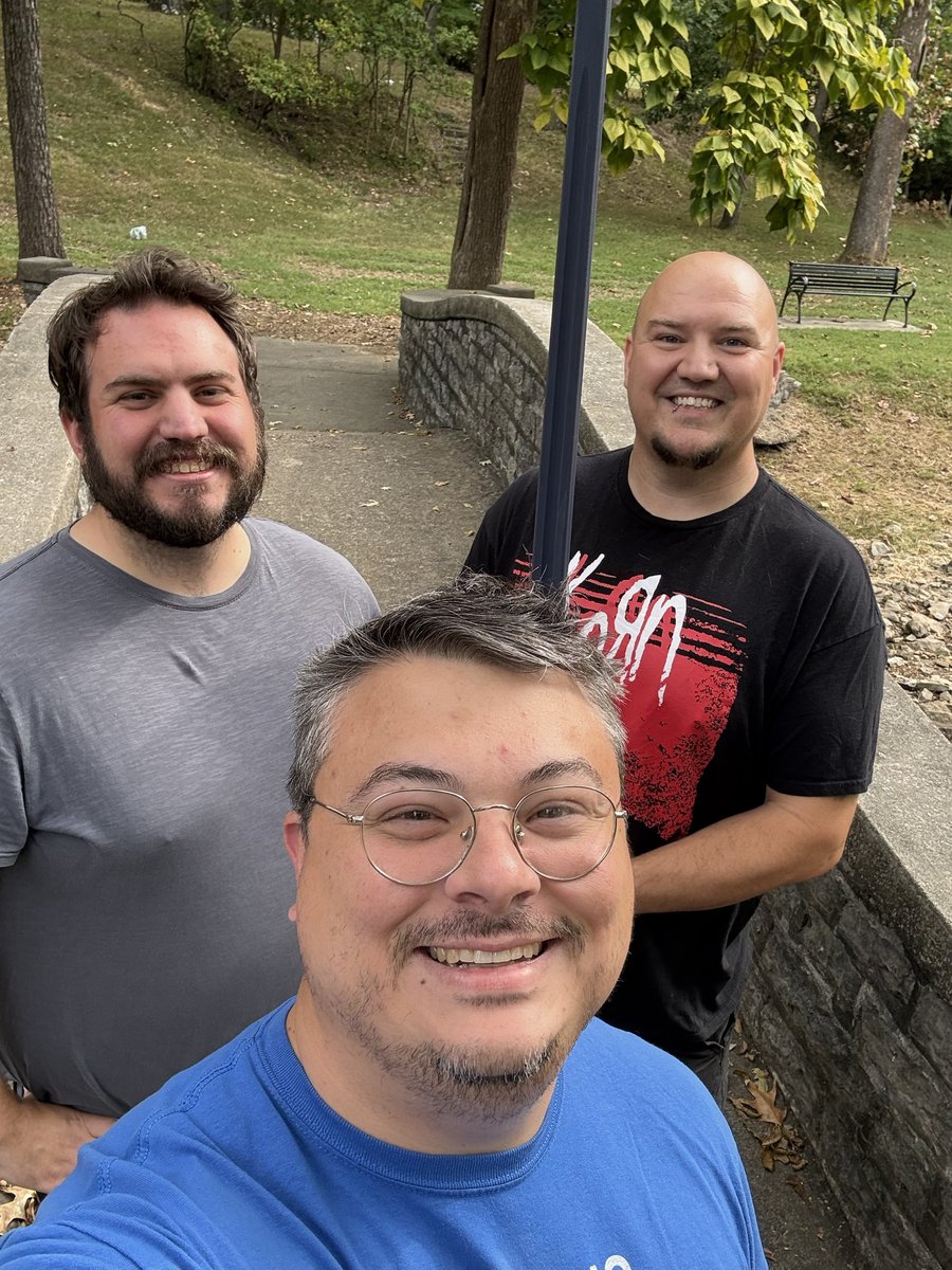 Three club members smiling together on a stone footbridge in a park